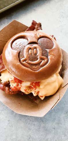 a mickey mouse sandwhich with bacon and cheese on it sitting in a cardboard box