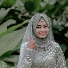 a woman wearing a hijab and holding her hand up to the side, smiling at the camera