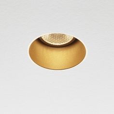 a white wall with a round light fixture on it's left side and a gold plated object in the middle