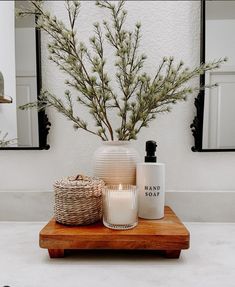 a wooden tray with candles and bottles on it in front of a white bathroom sink