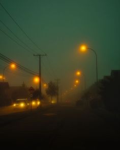 foggy street lights and cars driving down the road in the dark night time with no one on it