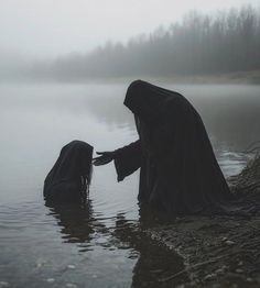 two people in black robes are standing in the water and touching hands with each other