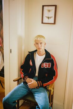 a young man sitting in a chair wearing a jacket