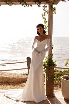 a woman in a white dress standing under a pergolated structure near the ocean