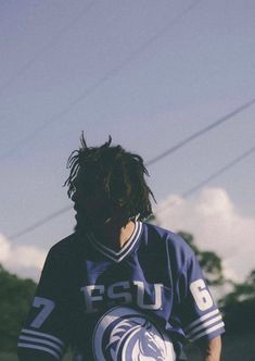 a young man with dreadlocks holding a skateboard in his hands and looking at the sky