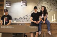 three young people sitting on top of a piano in front of a wall with an artistic design