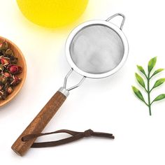 a tea strainer next to a wooden bowl filled with loose buds and lemons