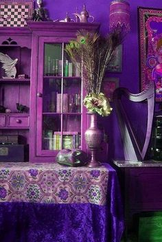 a room with purple walls and furniture in the corner, including a vase filled with flowers next to a harp