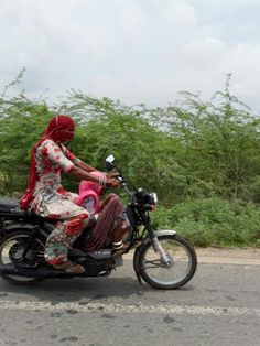 a woman riding on the back of a motorcycle down a road