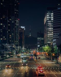 cars are driving down an empty city street at night with skyscrapers in the background