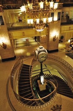 a clock on top of a spiral stair case in a building with chandelier