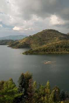 a large body of water surrounded by lush green hills and trees on the side of it