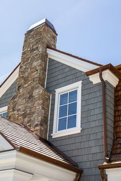 a gray house with white trim and a stone chimney on the roof, against a blue sky