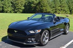 a black ford mustang convertible parked in a parking lot with trees in the back ground