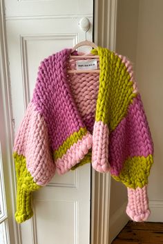 a pink, green and yellow sweater hanging on a door handle with a white door behind it