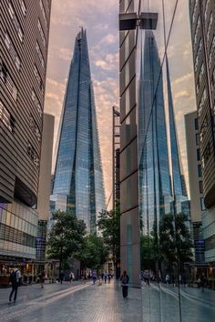 some very tall buildings near each other with people walking by them in the middle of the street