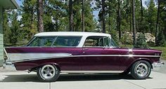 an old purple and white car parked in front of a house next to some trees