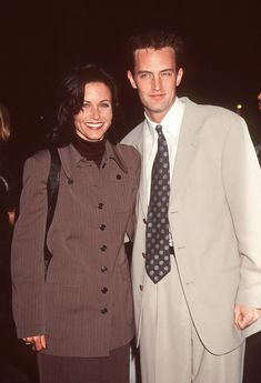 a man in a suit and tie standing next to a woman wearing a dress coat