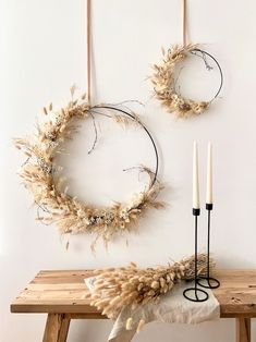 two wreaths are hanging on the wall next to a table with candles and some branches