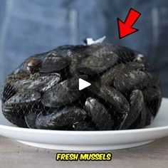 a white plate topped with black mussels on top of a wooden table next to a person