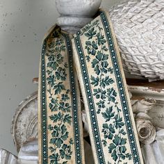 an old white vase sitting on top of a table next to a blue and green ribbon