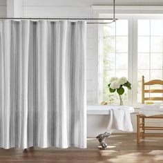 a white shower curtain in a bathroom next to a bathtub and chair with flowers on the floor