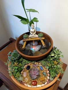 a buddha statue sitting on top of a bowl filled with water and rocks next to a plant