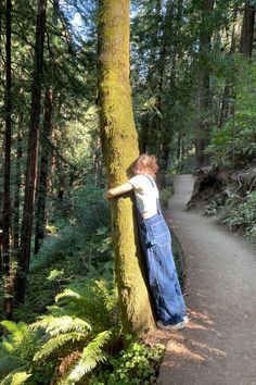 a person leaning against a tree in the woods with their arms on it's back