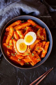 a bowl filled with carrots and an egg on top of it next to chopsticks