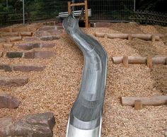 a slide that is in the middle of some wood chippings and gravel with rocks around it