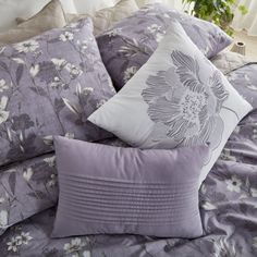 a bed covered in purple and white pillows next to a potted plant on a window sill