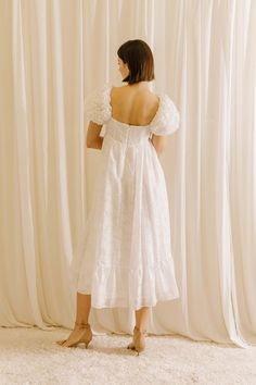 a woman standing in front of a curtain wearing a white dress with ruffles