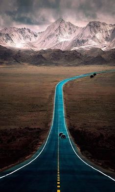 an empty road with mountains in the background and cars driving down one lane on both sides