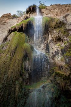 a waterfall with moss growing on the rocks and water running down it's sides