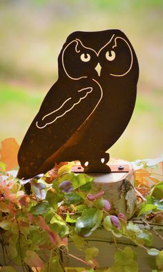 an owl statue sitting on top of a tree stump in front of some leaves and plants