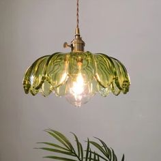 a green glass light hanging from a ceiling fixture next to a potted palm tree