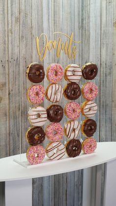 there are many donuts that are on the cake stand and it is decorated with gold lettering