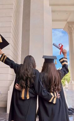 two girls in graduation gowns hold up their diplomas while they stand on the steps