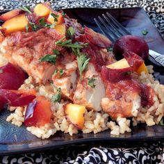 a black plate topped with rice and meat covered in veggies next to a fork