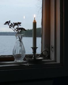 a candle is sitting on a window sill next to a vase with flowers in it