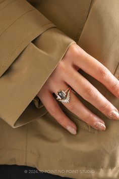 a woman's hand wearing a gold ring with a diamond on it and a tan trench coat