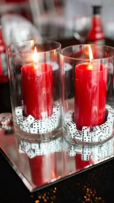 two red candles are sitting in glass cups on a table with silverware and other decorations