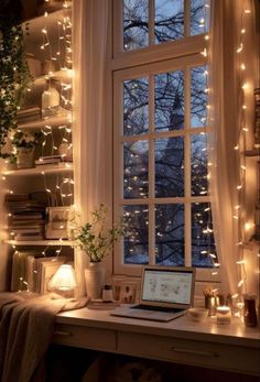 a laptop computer sitting on top of a desk next to a window covered in fairy lights