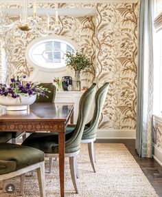 a dining room table with green chairs and a white vase filled with flowers on top of it