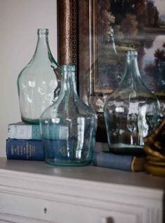 three glass vases sitting on top of a white dresser next to a framed painting