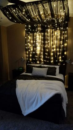 a bed that has some lights on the headboard and curtains over it in front of a window