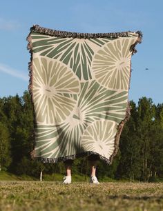 a person standing under a large blanket in the middle of a field with trees behind them