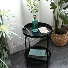 a small table with some books and flowers on it next to a potted plant