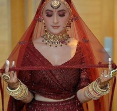 a woman in a red bridal outfit holding something up to her face