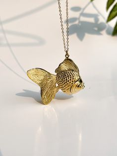 a gold fish necklace sitting on top of a white table next to a potted plant